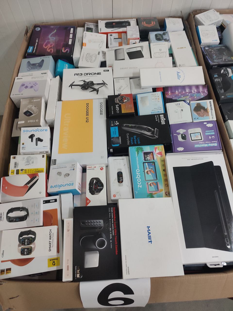Real pallet of returned electronics — drones, smartwatches, earbuds, speakers